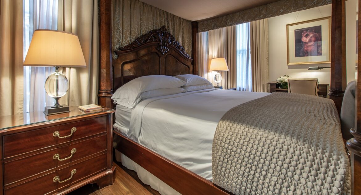 Hinman Suite canopy bed with a wood nightstand and lamp on top