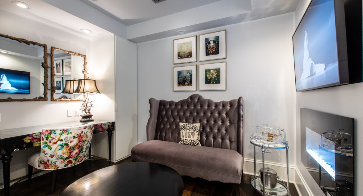 tufted velvety loveseat with lust pillow in lovely decorated bedroom with wood floors, desk with floral chair and mirrors - Stedman Suite at Stonehurst Place