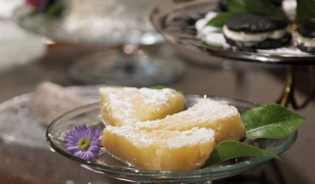 yellow dessert pie with powdered sugar on glass cake plate with other desserts in background