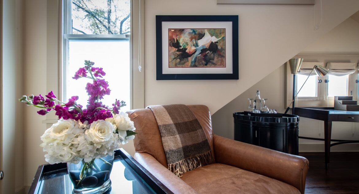 The Gables room leather arm chair with a side table and glass vase with flowers on top