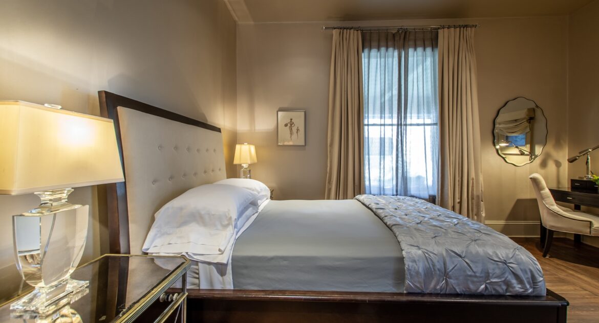 Farnsworth room with mirrored nightstand and bend with grey sheets and silver metallic comforter