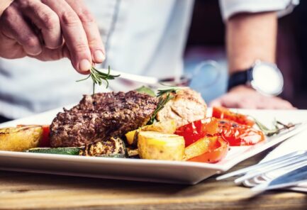 Chef in hotel or restaurant kitchen cooking only hands. Prepared beef steak with vegetable decoration.